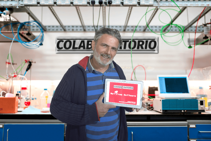 aldobelus, rodeado de aparatos de laboratorio, muestra un cartel con el texto: "We love Free Software" y el logotipo de Colaboratorio.